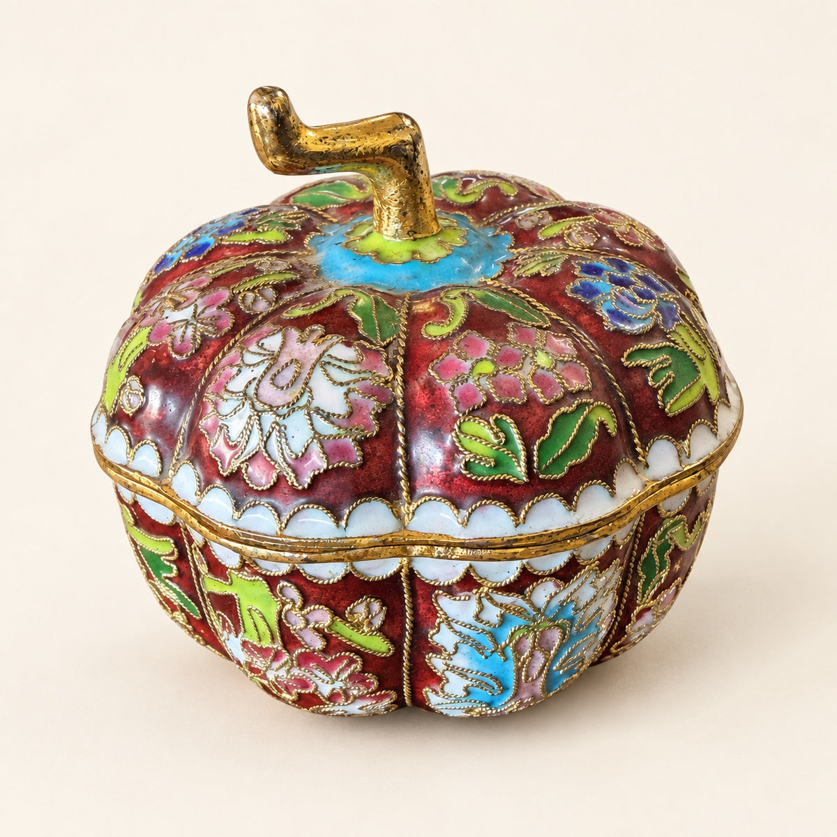 An ornate pumpkin-shaped decorative box with a lid, decorated in red, pink, green, and blue floral enamel with gold metal trim and a gold stem, set against a plain cream background.