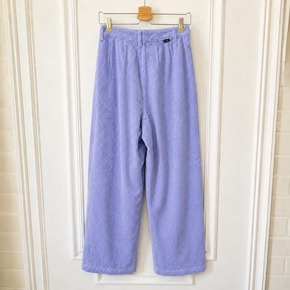 Light purple corduroy wide-leg cropped pants hanging on a wooden hanger against a white paneled door.