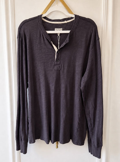 A dark charcoal gray long-sleeve henley shirt hanging on a wooden hanger against a white paneled door.