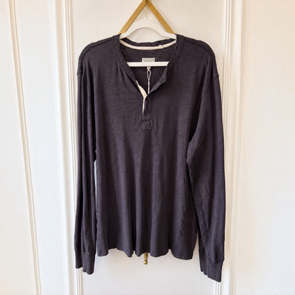 A dark charcoal gray long-sleeve henley shirt hanging on a wooden hanger against a white paneled door.