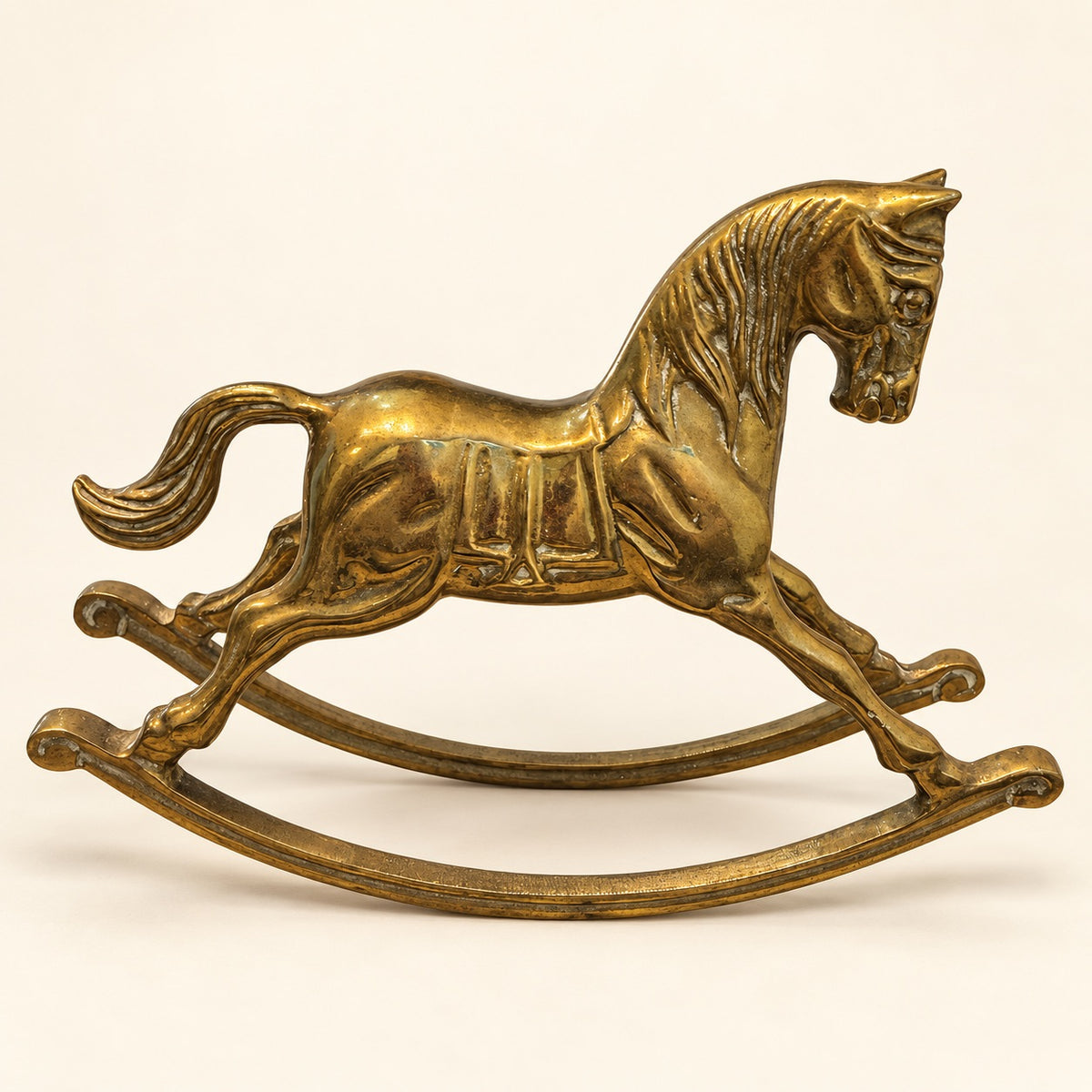 A small metallic rocking horse figurine in an antique gold or brass finish, photographed against a plain light beige background.