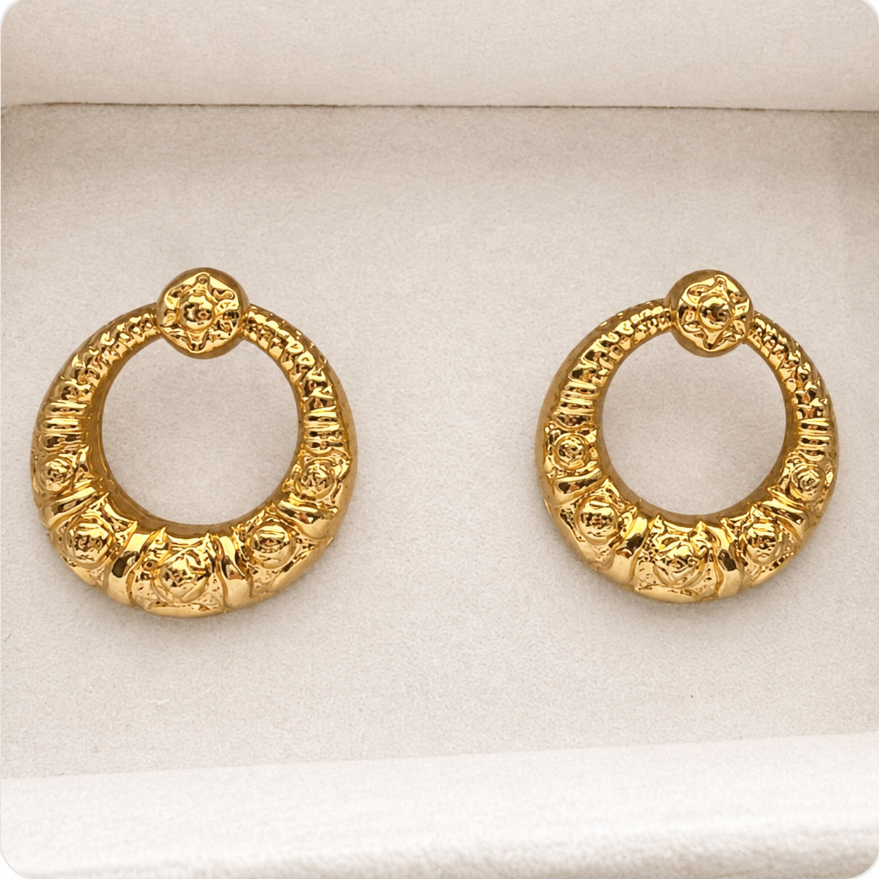 A pair of textured gold huggie hoop earrings displayed on a white velvet jewelry box.
