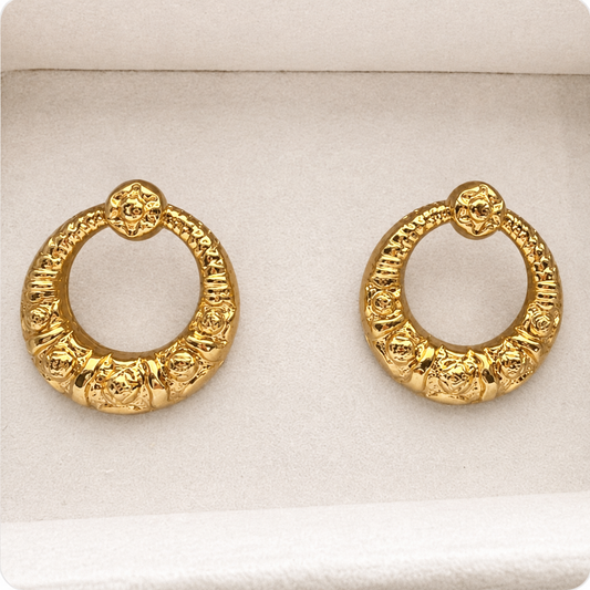 A pair of textured gold huggie hoop earrings displayed on a white velvet jewelry box.