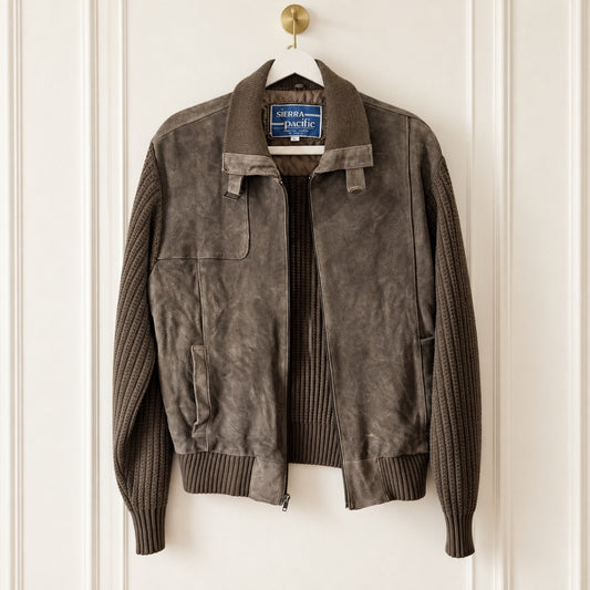 A dark brown suede jacket with ribbed knit sleeves and collar, hanging on a white hanger against a white paneled door. The brand label reads 'serpentine & Pacific'.