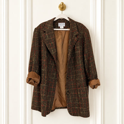 A brown plaid wool blazer with a tan lining, hanging on a white hanger with a gold ring pull against a white paneled door.