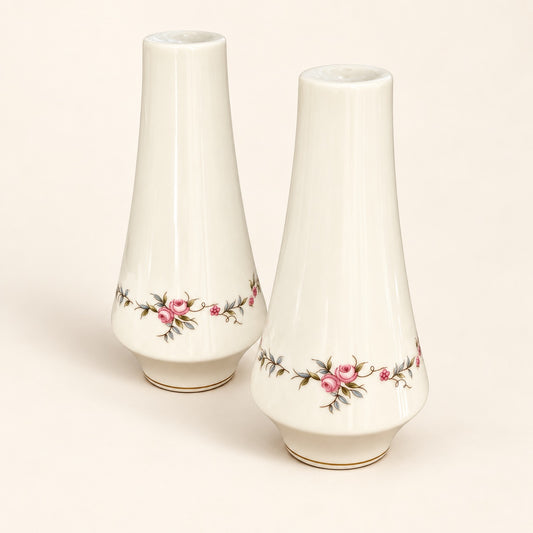 Two white ceramic vases with a delicate pink and green floral border design near the base, displayed on a warm cream background.