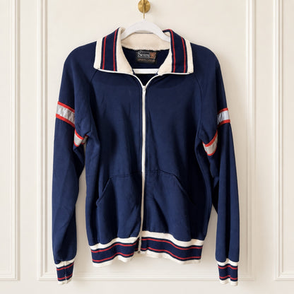 A vintage navy blue zip-up track jacket with white and red striped ribbed trim, hanging on a white hanger against a white paneled door.