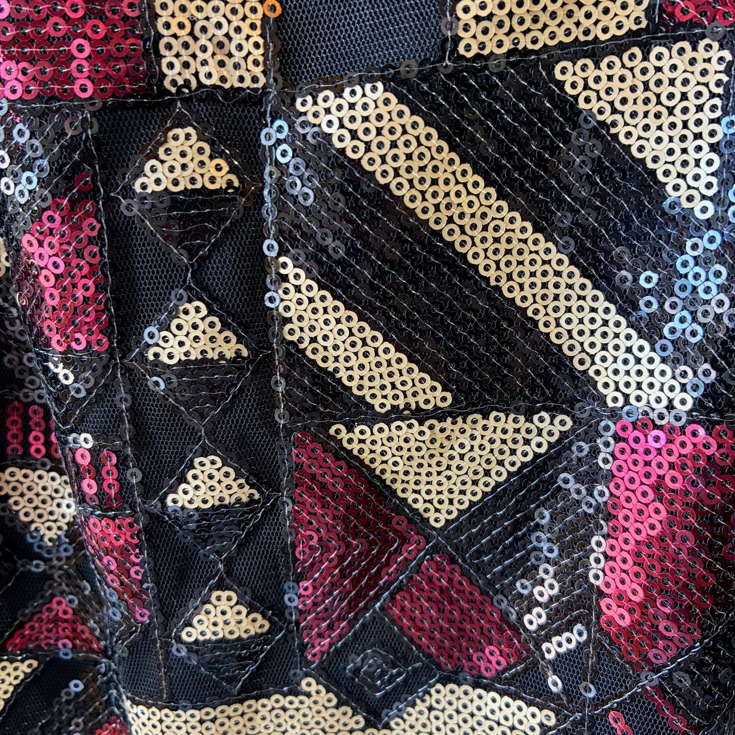 Close-up of a geometric sequined textile pattern featuring black mesh, beige sequins, and pink sequins in triangular and diagonal block designs.