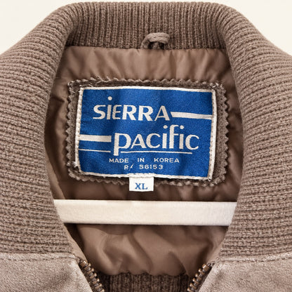Close-up of the interior collar and neck label of a brown ribbed knit jacket. The blue and white woven label reads 'SIERRA PACIFIC' with 'MADE IN KOREA' and a small size tag reading 'XL'.