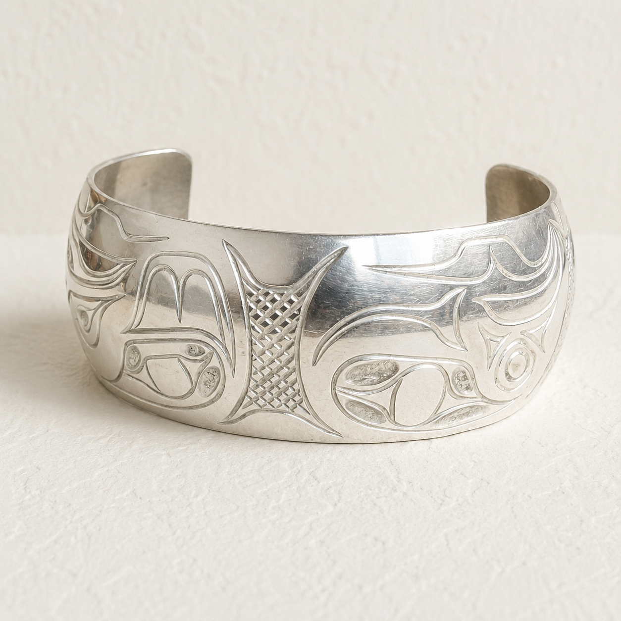A wide sterling silver cuff bracelet with engraved orifices and abstract carvings, photographed on a textured off-white background.