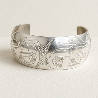 A wide sterling silver cuff bracelet with engraved orifices and abstract carvings, photographed on a textured off-white background.