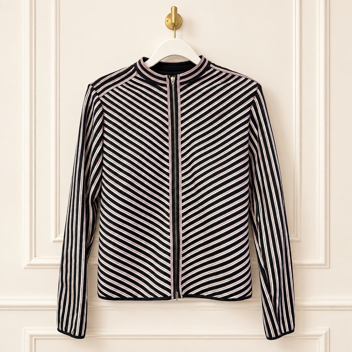 A women's zip-front jacket with a stand collar, featuring diagonal black and white stripes on the body and sleeves, hanging on a white hanger against a cream-colored paneled wall.