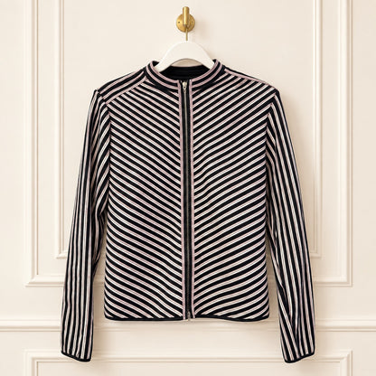 A women's zip-front jacket with a stand collar, featuring diagonal black and white stripes on the body and sleeves, hanging on a white hanger against a cream-colored paneled wall.
