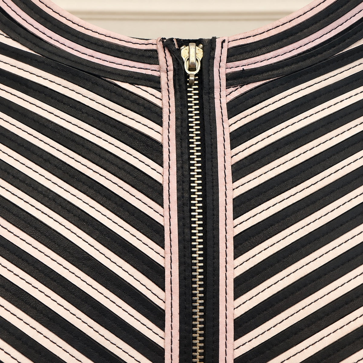 Close-up of a garment's neckline featuring diagonal black, white, and light pink stripes, finished with a central gold zipper.