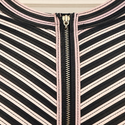 Close-up of a garment's neckline featuring diagonal black, white, and light pink stripes, finished with a central gold zipper.