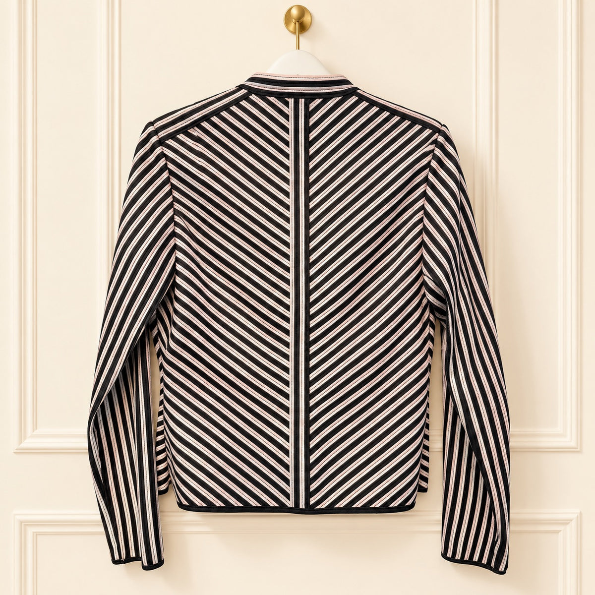 A long-sleeve striped jacket hanging on a white hanger against a cream-colored paneled door. The jacket features a bold diagonal stripe pattern in black and off-white, with a solid black center panel running down the back.