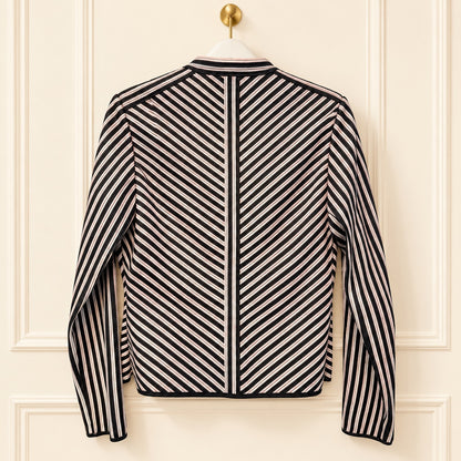 A long-sleeve striped jacket hanging on a white hanger against a cream-colored paneled door. The jacket features a bold diagonal stripe pattern in black and off-white, with a solid black center panel running down the back.