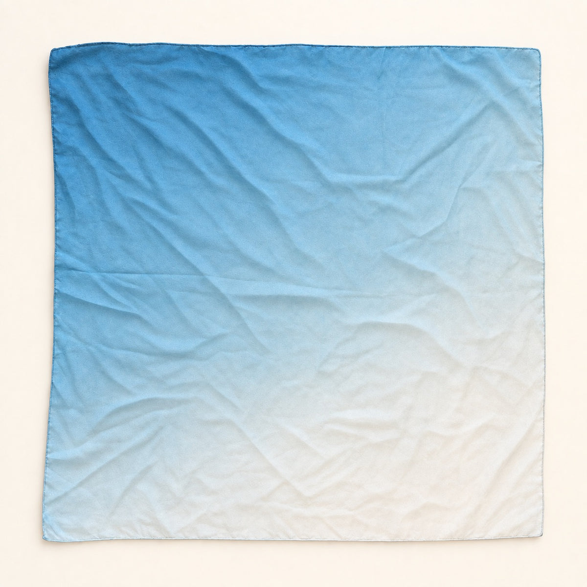 A square fabric scarf with a smooth blue-to-white gradient ombre design, laid flat on a light cream background.