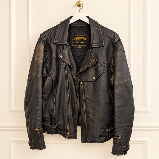 A black leather motorcycle jacket hanging on a white hanger against an off-white paneled wall. The jacket has a vintage distressed finish with visible wear and tear, gold-toned zippers, and a brand label inside the collar reading 'Ride Lite'.