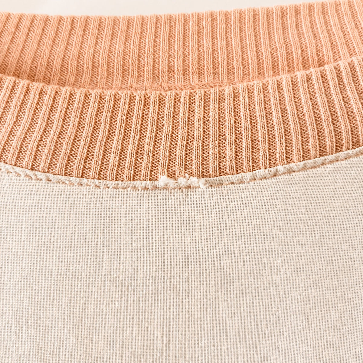 Close-up of a ribbed knit crew neck sweater showing two color options: a peachy orange ribbed collar over a light beige body.