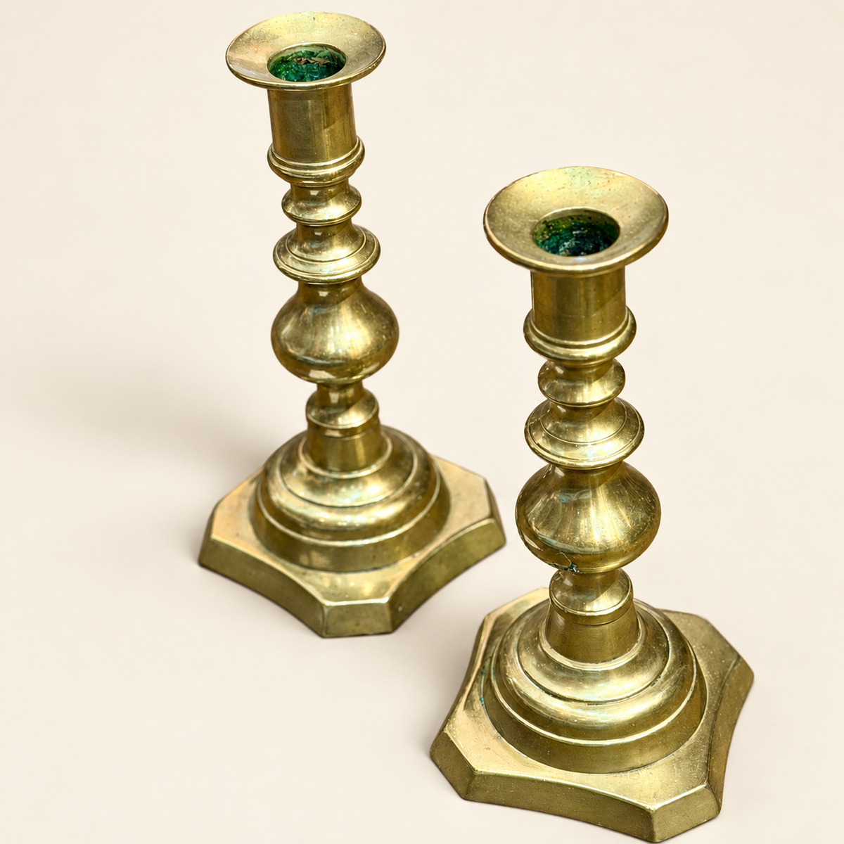 A pair of vintage brass candlesticks with tiered stems and hexagonal bases, shown on a plain light beige background.