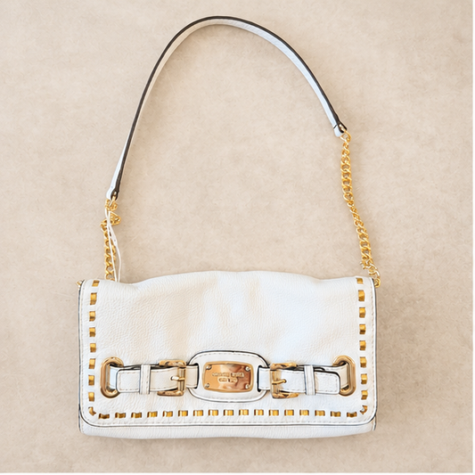 A white pebbled leather shoulder bag with gold-tone hardware, featuring a curved top handle, a gold chain strap, and a decorative front strap detail with gold studs, set against a neutral beige background.