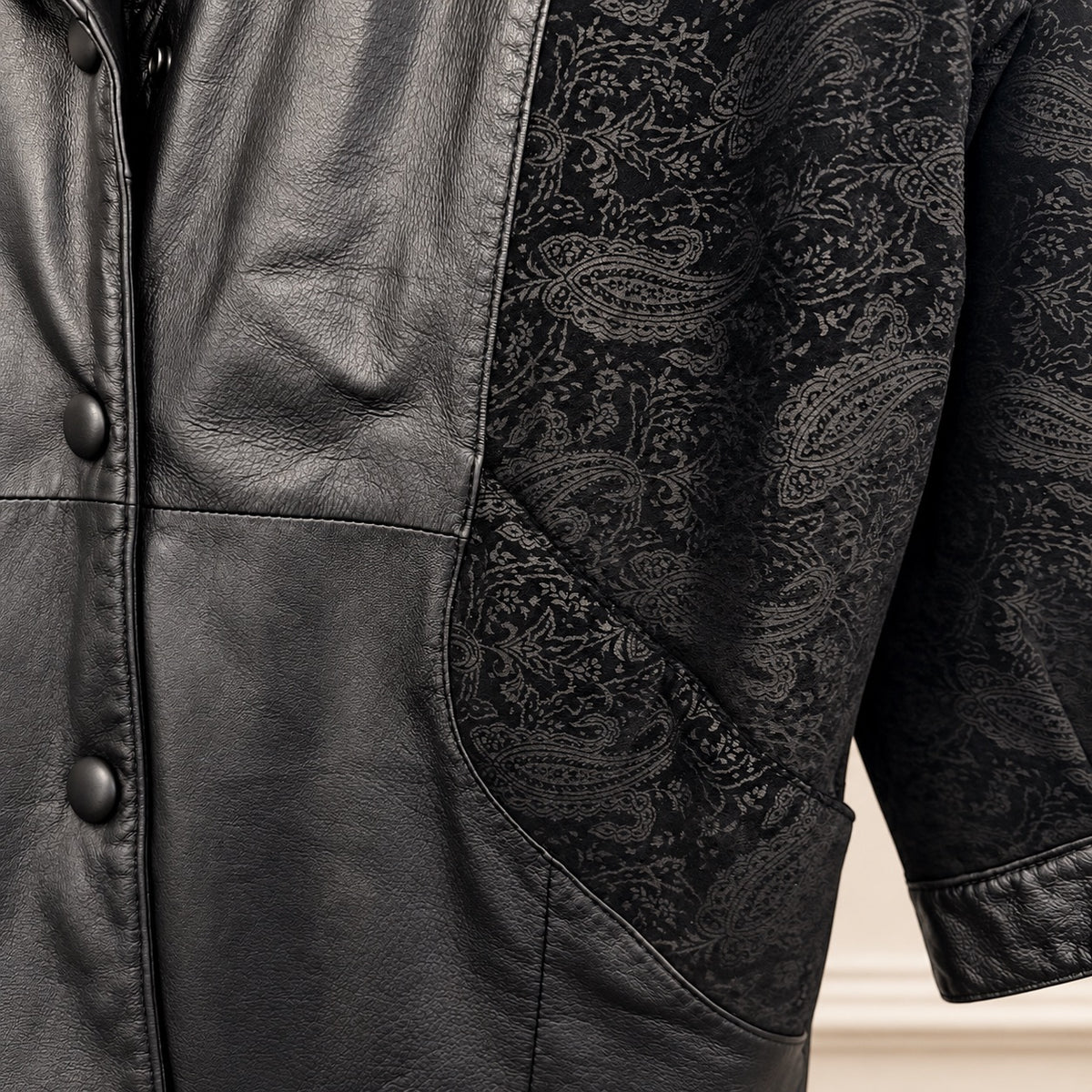 Close-up of a black leather jacket with contrasting black paisley brocade fabric panels on the sleeves and side.