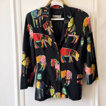 A black blazer jacket featuring a vibrant, multicolored zebra print, hanging on a wooden hanger against a white paneled door.