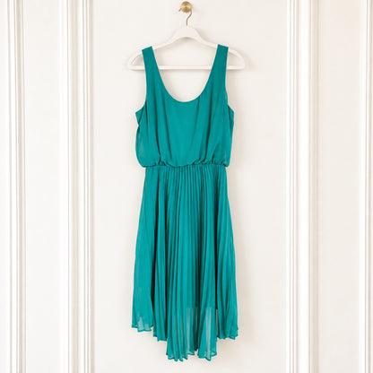 A sleeveless teal green dress with a scoop neckline and a pleated skirt, hanging on a white wooden hanger against a white paneled wall.
