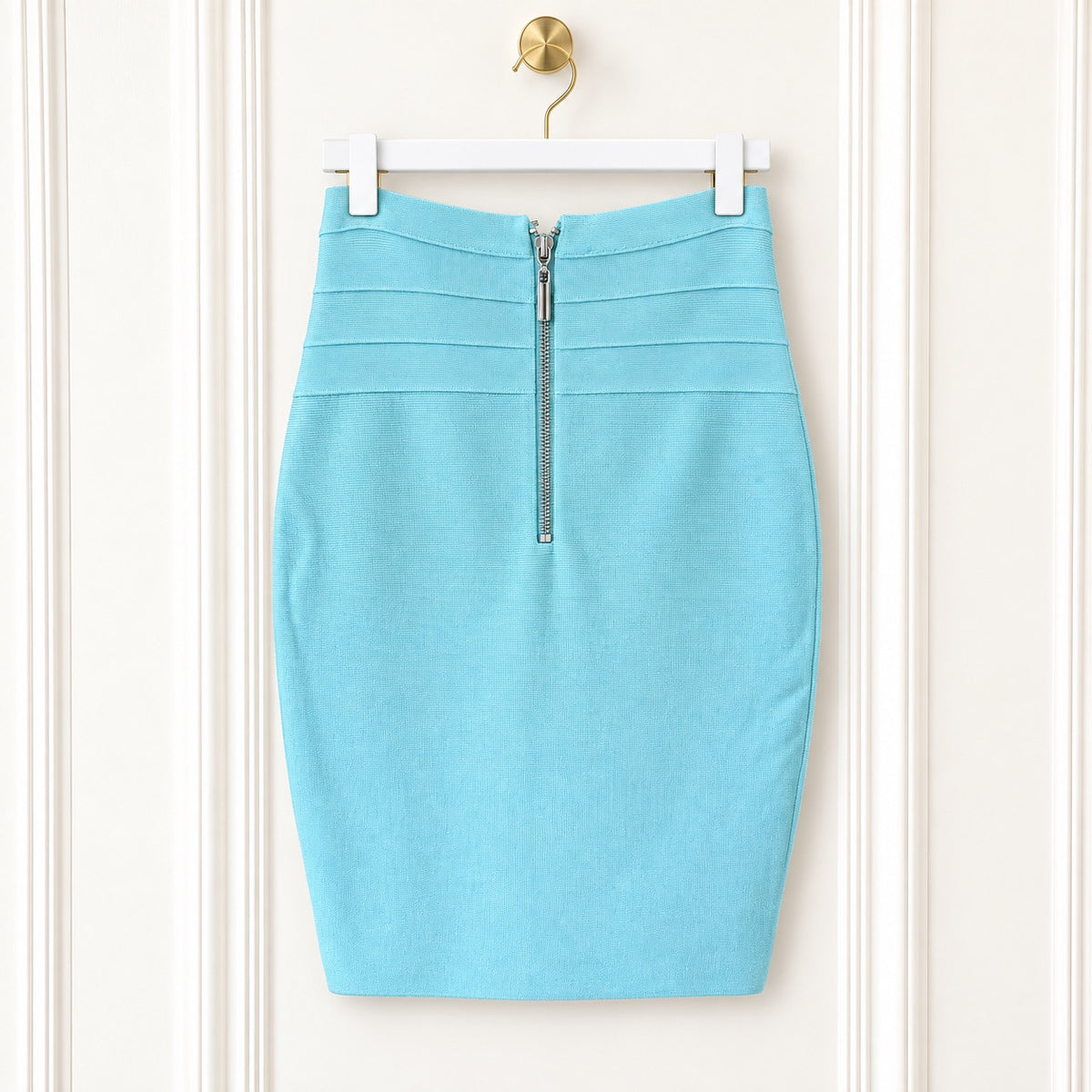 A light blue pencil skirt with a front zipper, hanging on a white hanger against a cream-colored paneled door.