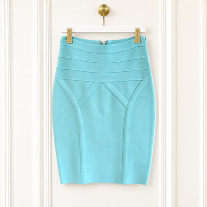 A light blue pencil skirt with structured paneling and diagonal seam details, hanging from gold clips on a white hanger against a white paneled door.