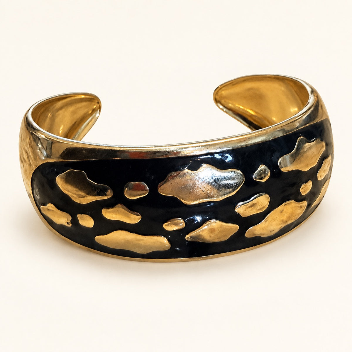 A wide open cuff bracelet featuring a glossy black enamel center with irregular raised gold metallic inlays, photographed on a clean off-white background.