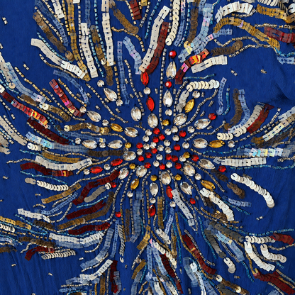 A close-up of a royal blue fabric featuring an intricate, radial embroidered and beaded pattern in metallic gold, silver, red, and brown tones.