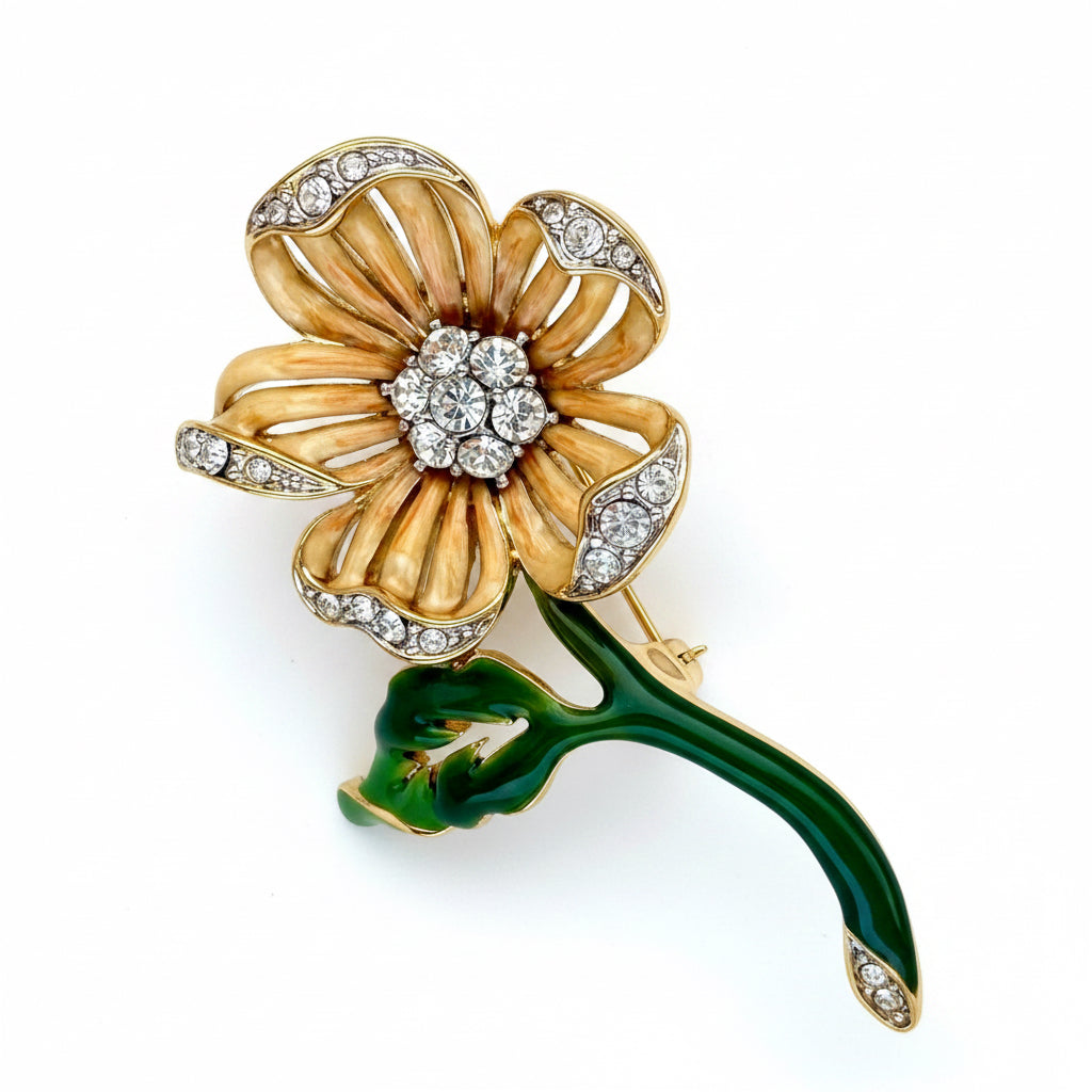 A gold flower-shaped brooch with green enamel leaves, set with clear crystals, displayed on a neutral beige background.