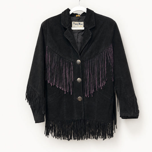 A black suede fringe jacket with purple fringe accents on the chest, hanging on a white hanger against a plain white wall. The brand label reads 'Pierce Wear'.