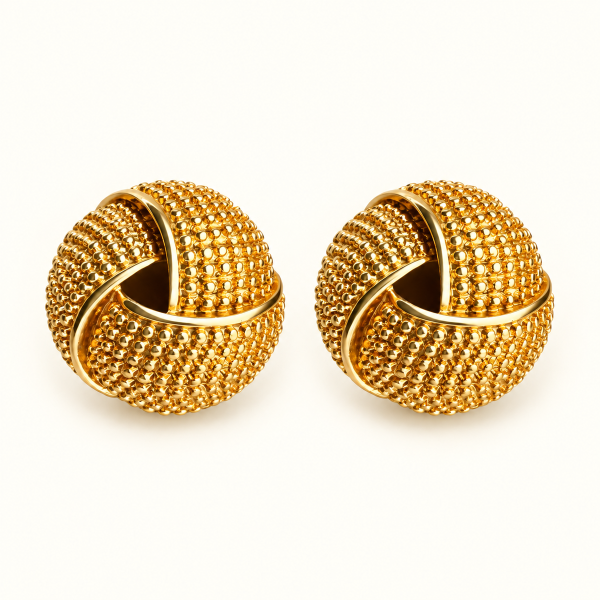 A pair of gold-toned knot-style earrings with a textured, beaded surface, displayed on a clean white background.
