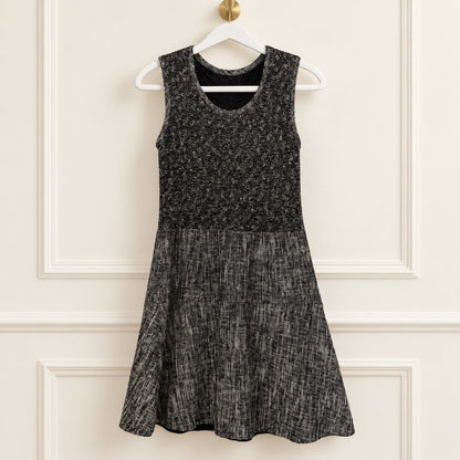 A sleeveless black and gray textured dress hanging on a white hanger against a cream-colored paneled wall.