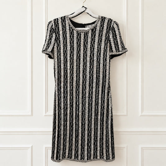 A short-sleeve black and white vertically patterned dress hanging on a black hanger against a white paneled wall.