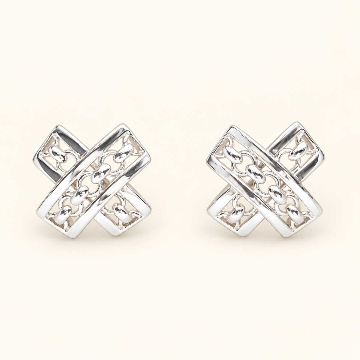 A pair of silver-toned geometric stud earrings with an interlocking cross design and openwork detailing, displayed on a light cream background.