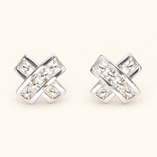 A pair of silver-toned geometric stud earrings with an interlocking cross design and openwork detailing, displayed on a light cream background.