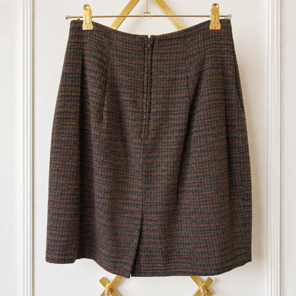 A vintage plaid skirt in brown, red, and black wool, hanging on a gold metal hanger against a white paneled wall.